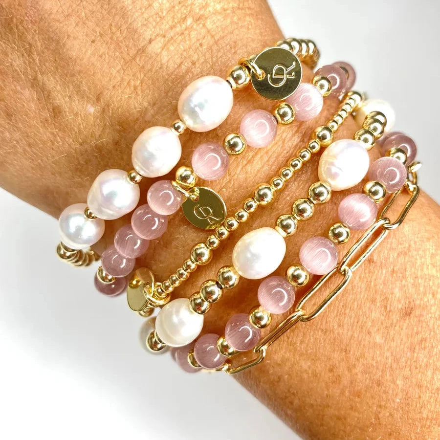 Stack of pink beaded bracelets with gold accents on a wrist against a white background